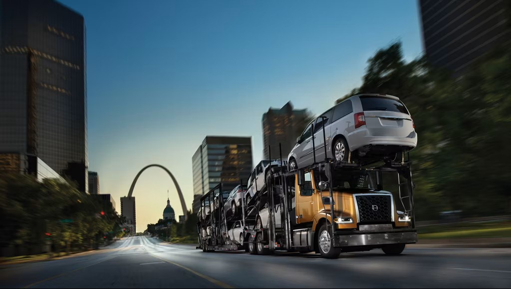 Car-hauler semi-truck transporting passenger vehicles on a St. Louis highway with the Gateway Arch and downtown skyline in the background